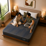A couple sits on a dark gray Euro Top Hybrid Latex Pocket Spring Mattress on a wooden bed frame in a warmly lit bedroom. The mattress has a visible Springfree label near the bottom edge.